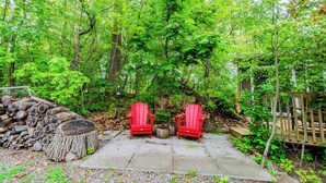 Eine Terrasse mit zwei roten Adirondack-Stühlen, einem Feuerkorb und einem Holzstoß.