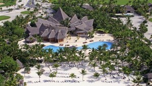 A resort with multiple thatched-roof buildings, a central pool, and surrounding palm trees.