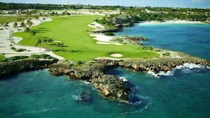 A coastal golf course with a clear view of the ocean, a sandy beach, and a rocky shoreline.