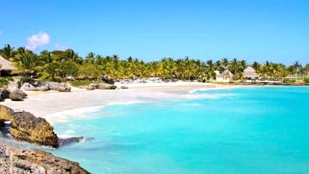A beach resort with clear turquoise waters, palm trees, and thatched-roof huts.