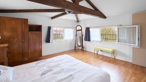 Un dormitorio con vigas de madera, una cama, un armario, un banco y ventanas con cortinas.
