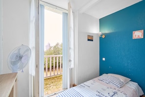Quarto com cama, ventilador, porta que dá para uma varanda externa e parede azul com decoração náutica.