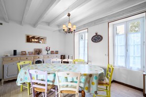 Uma sala de jantar com uma mesa redonda, cadeiras, um candelabro, um relógio e uma janela com cortinas.