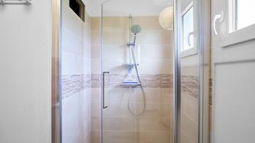 A glass-enclosed shower with a handheld showerhead and a wall-mounted faucet.