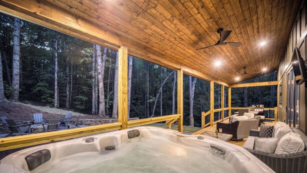 Un jacuzzi con cubierta de madera y zona de estar al aire libre, rodeado de altos árboles.