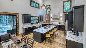 Una cocina moderna con una isla grande, armarios oscuros y ventanas amplias.
