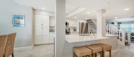 A modern kitchen with white cabinetry, a central island, and a dining area with wicker stools.