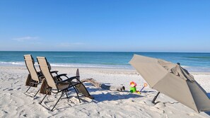 A beach with two beach chairs and a beach umbrella on the sand.