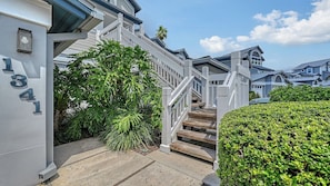 A residential building with a staircase leading to a porch, surrounded by greenery and a well-maintained hedge.