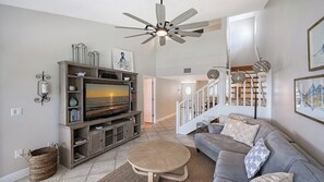 A living room with a TV, sofa, and a staircase leading to another level. - Heated Pool, FREE WIFI Luxury Bayside Condo Across from Siesta Key Beach |  Beautiful 3BR/2BA Gulf & Bay Club Bayside Condo (Sarasota)