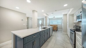 A modern kitchen with a central island, built-in appliances, and a dining area with a ceiling fan. - Heated Pool, FREE WIFI Luxury Bayside Condo Across from Siesta Key Beach | Beautiful 3BR/2BA Gulf & Bay Club Bayside Condo (Sarasota)
