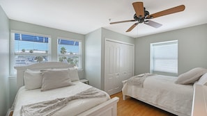A bedroom with two beds, a ceiling fan, and large windows with blinds.