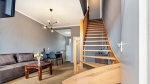 Ein modernes Wohnzimmer mit einer Holztreppe, einem Sofa, einem Couchtisch und einem Essbereich im Hintergrund.