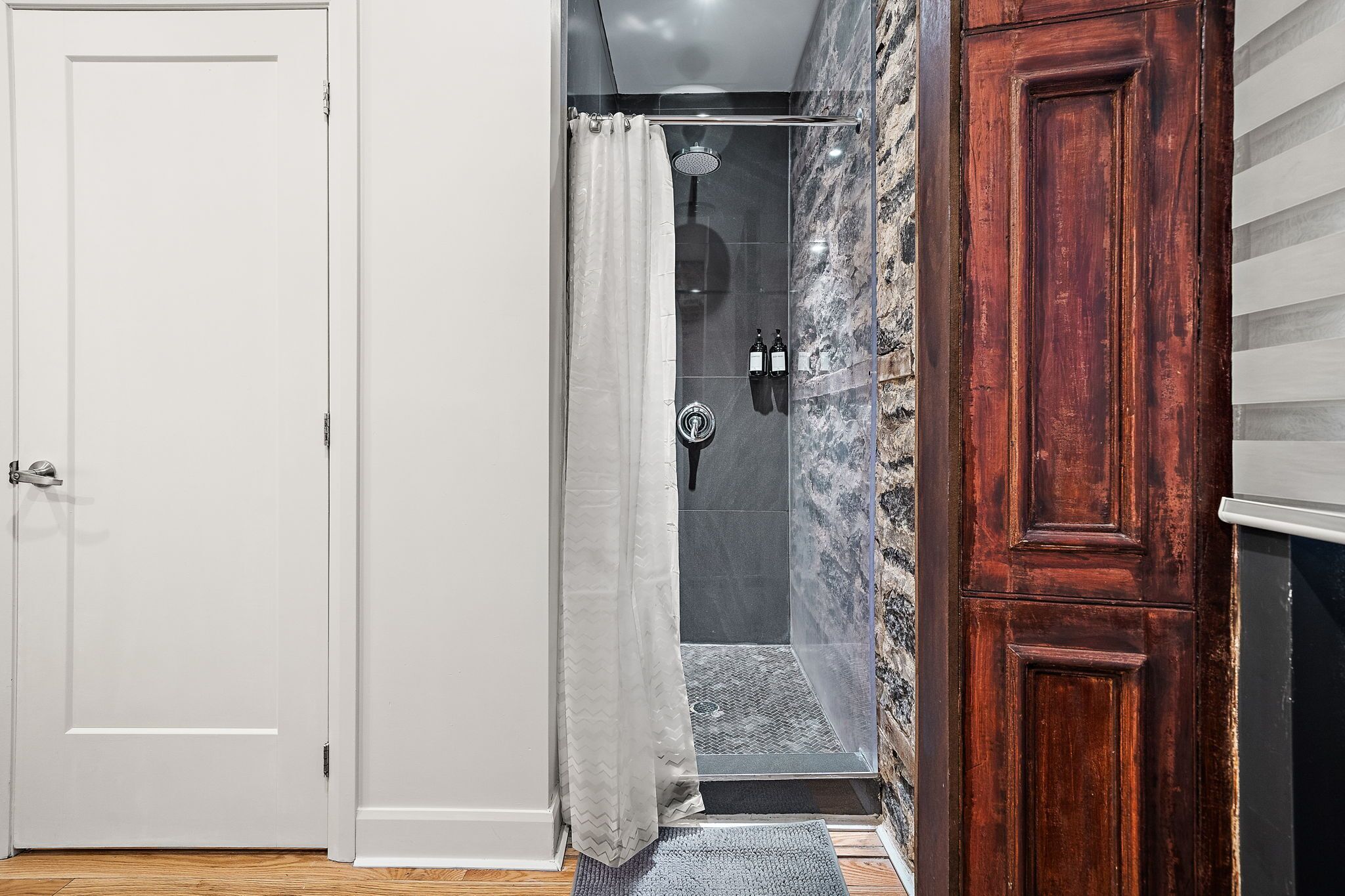 Ein Badezimmer mit Dusche, einer Holztür und einer Marmorwand.