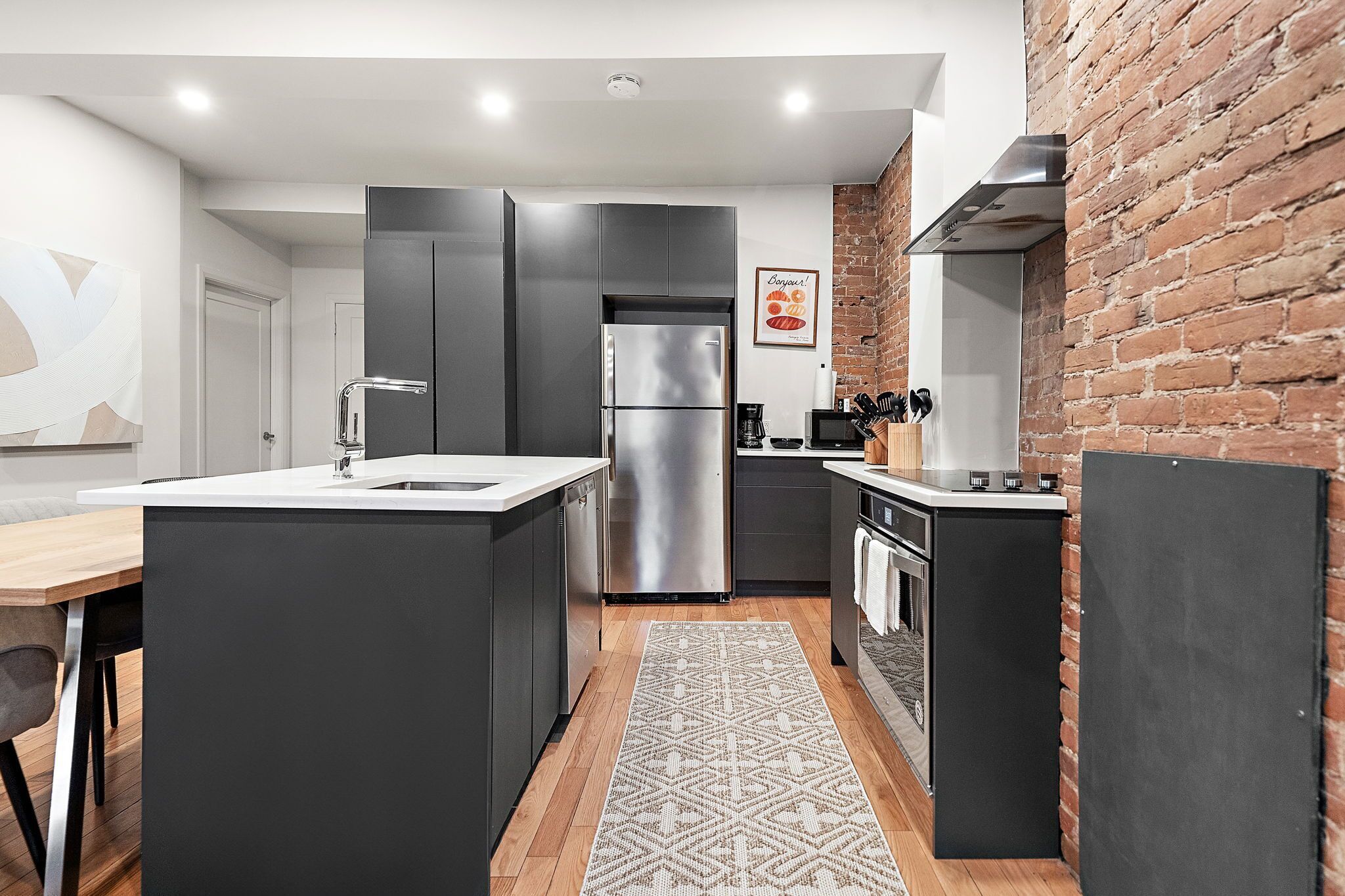 Una cocina moderna con una isla central, electrodomésticos de acero inoxidable y una pared decorativa de ladrillo.