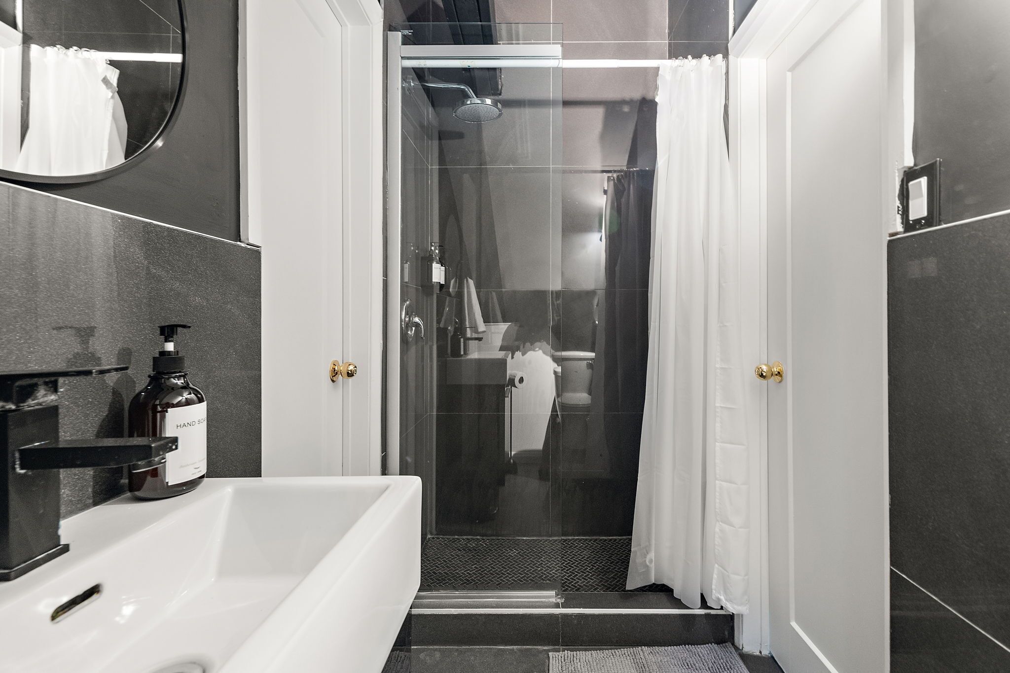 Ein modernes Badezimmer mit einer gläsernen Duschkabine, einem großen Spiegel und einer weißen Badewanne.