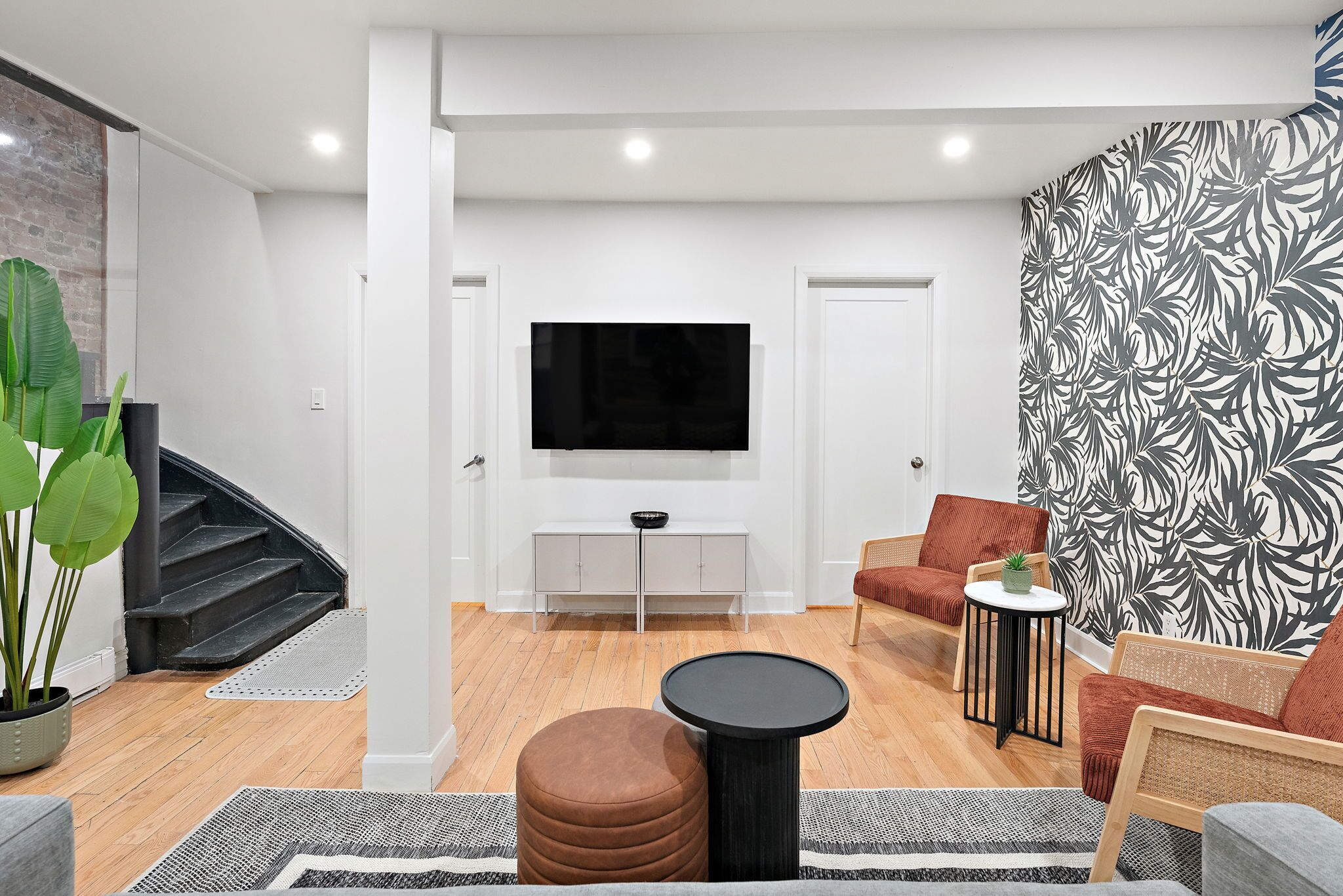 A modern living room with a staircase, a flat-screen TV, a white console table, and patterned wallpaper.