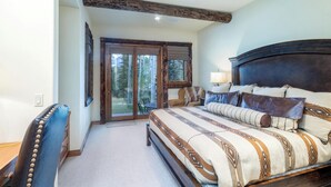 A bedroom with a large bed, a wooden headboard, a chair, and a view of a forest through a glass door.