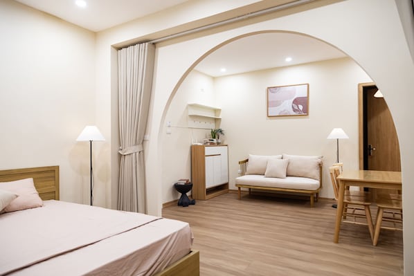 A hotel room with a bed, a desk, a sofa, a lamp, a plant, and a painting on the wall.