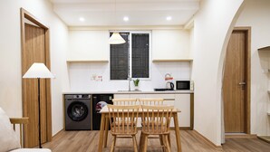 A compact kitchen with a washing machine, a dining table with chairs, and a microwave. - Fully Equipped 2BR/2BA Apt Old Quarter & Hoan Kiem (Hà Nội)