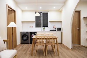 A compact kitchen with a washing machine, a dining table with chairs, and a microwave.