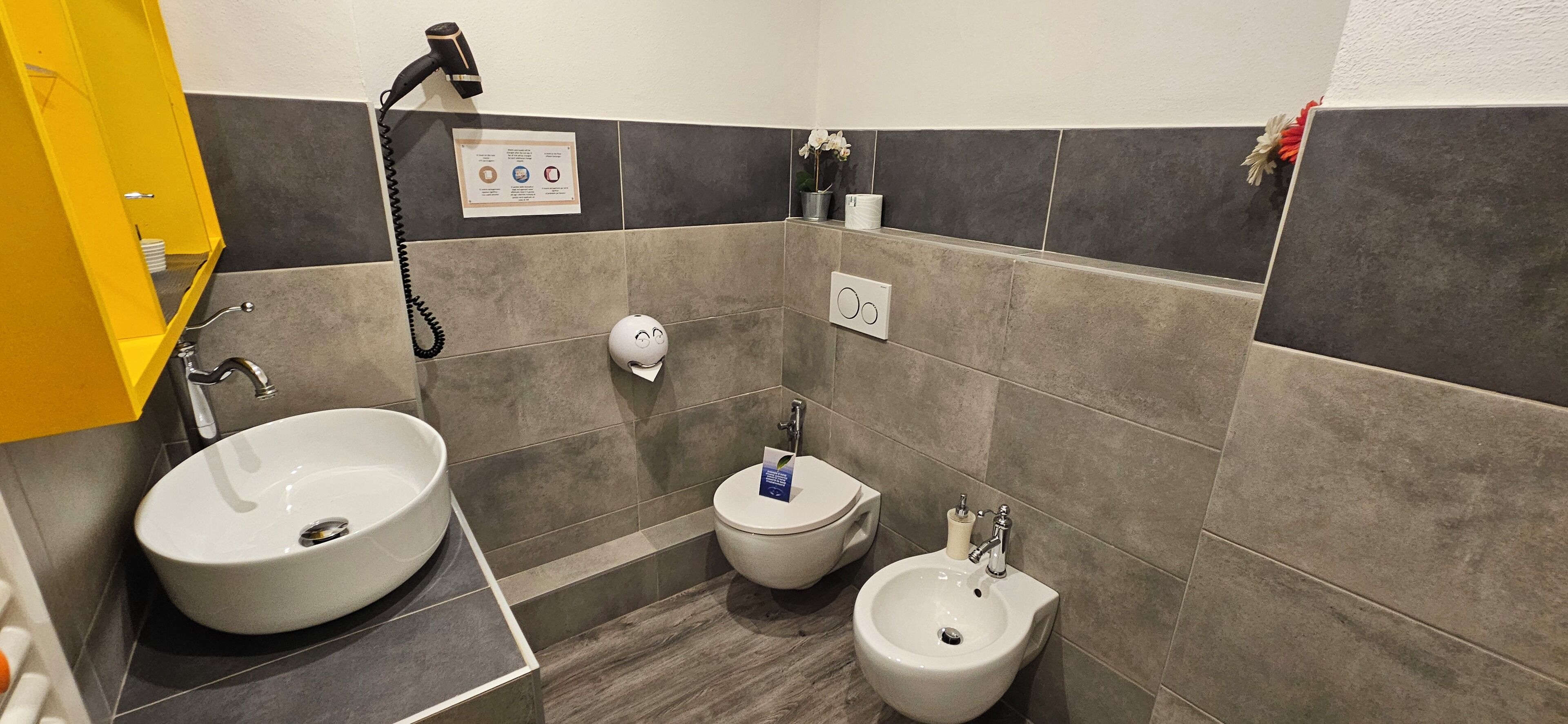 Un baño con un lavabo grande, dos inodoros, un bidé y un armario amarillo.