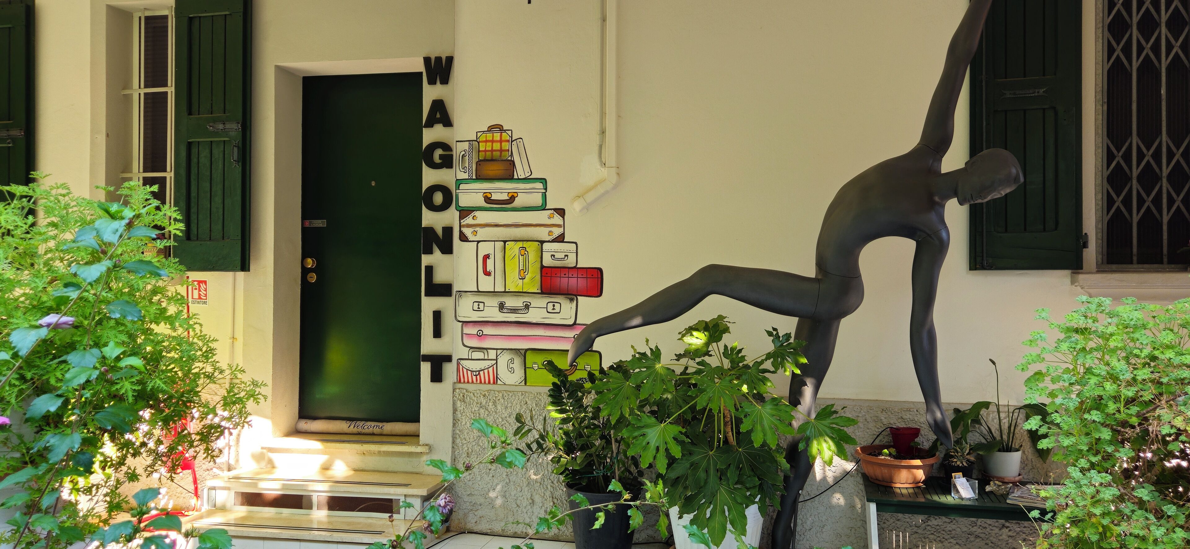 Una habitación con una puerta verde, una pila de maletas y una estatua de una persona.