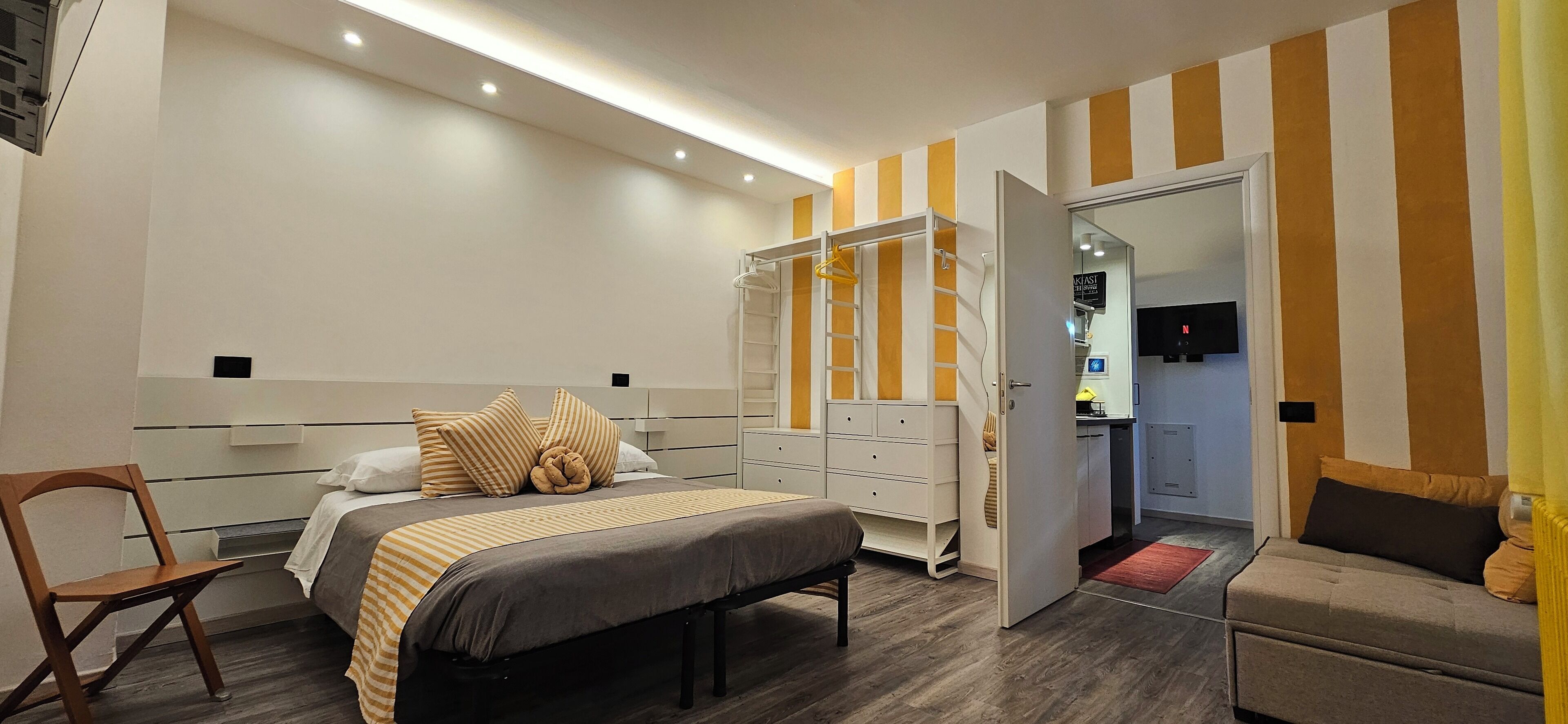 A bedroom with a bed, bedside table, chair, wardrobe, and a mirror.