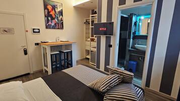 Ein Hotelzimmer mit Bett, Schreibtisch mit Stuhl, Wandfernseher, Badezimmer mit Waschbecken und Spiegel sowie Streifenmuster an den Wänden.