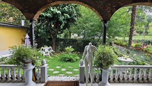 An outdoor garden area with a statue, a yellow wall, and a brick archway. - Wagon-lit (Bologna)