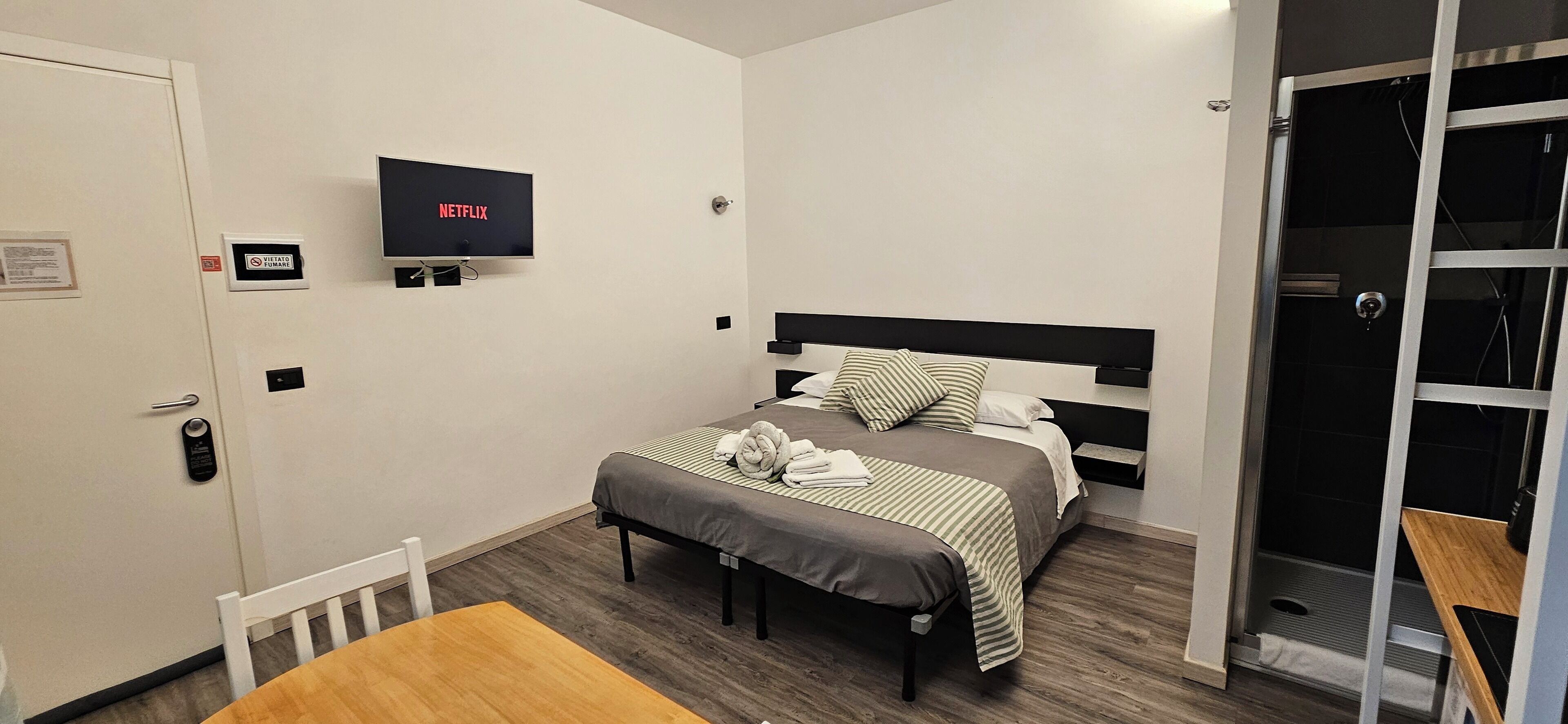 A hotel room with a bed, a TV mounted on the wall, a wooden table, and a door with a sign.