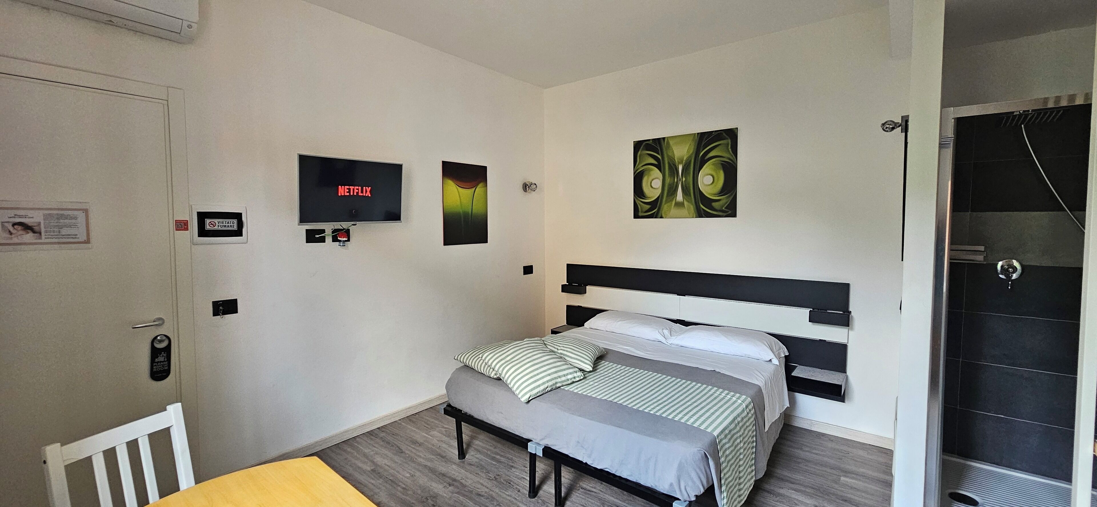 Un dormitorio con una cama, un televisor montado en la pared y una puerta con un cartel.
