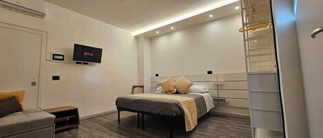 A modern hotel room with a bed, a TV mounted on the wall, a small table, and a built-in closet.
