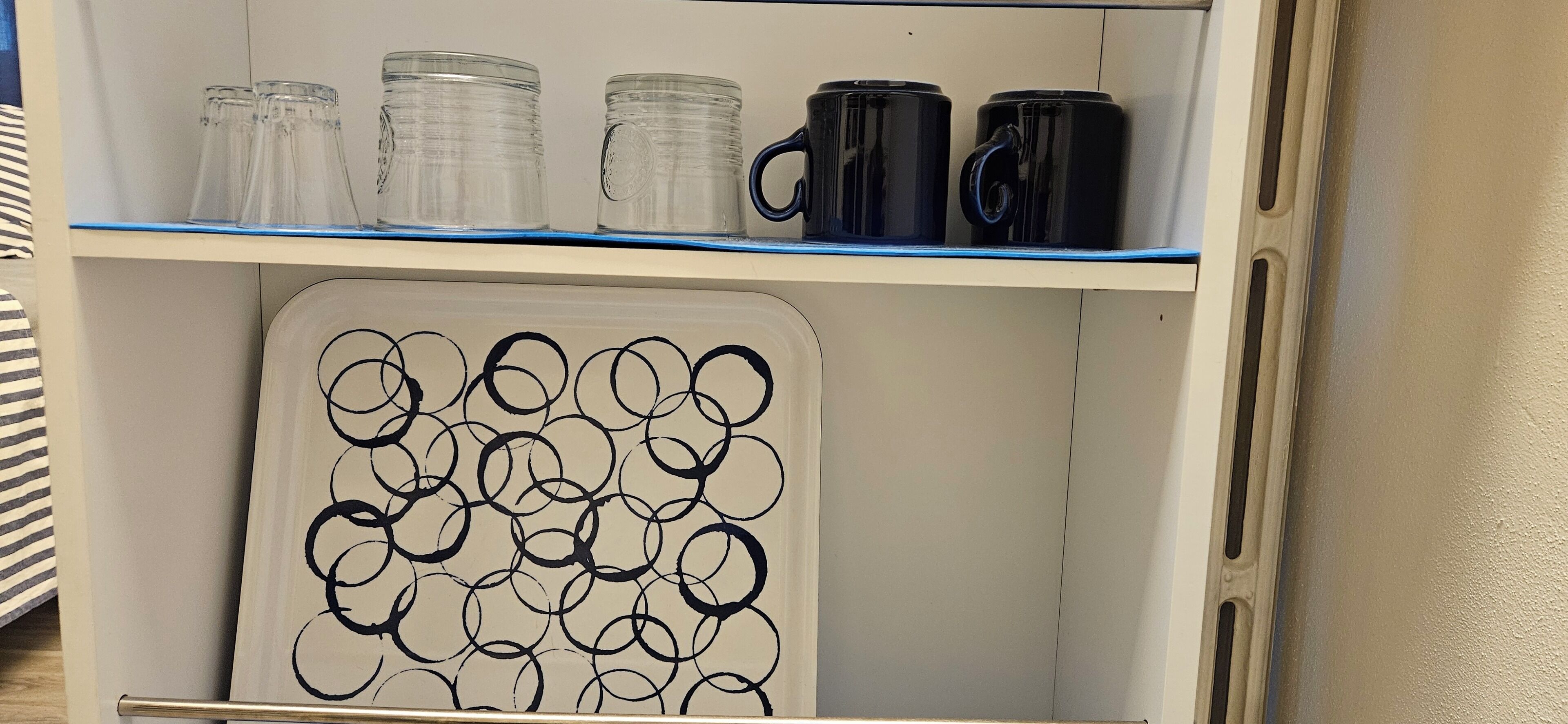 Un meuble de rangement doté d’étagères où sont disposés divers récipients en verre et des tasses noires.