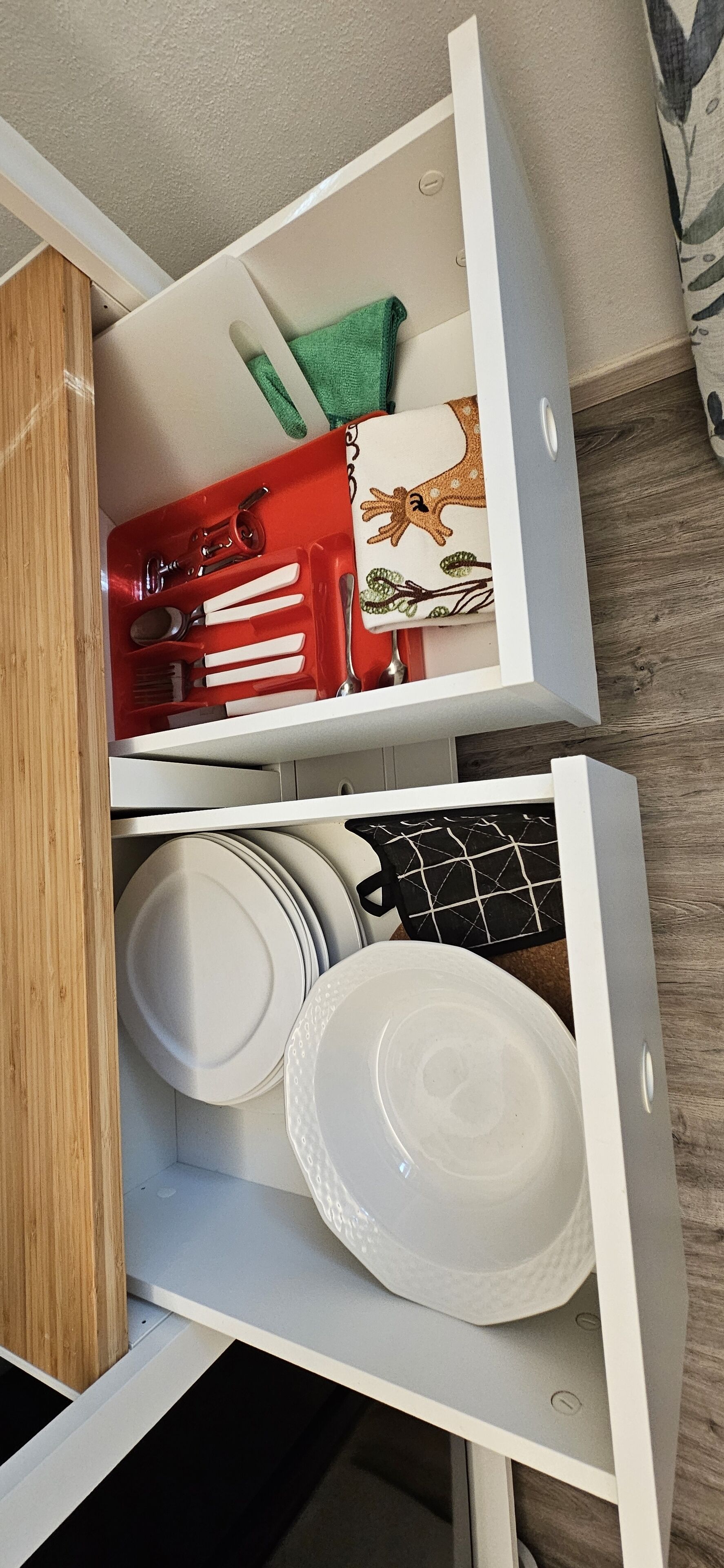 A kitchen drawer with white plates, a black pot, and a red utensil organizer.