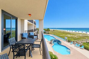 A balcony with a table and chairs, overlooking a swimming pool and beach. - Phoenix East 203 – Gulf-front with pool views & resort amenities (Orange Beach)