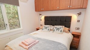 Una cama bien hecha con edredón gris y beige, dos almohadas con diseños de mariposas y una toalla rosa sobre la cama.