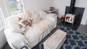 Una habitación acogedora con un sofá blanco, una chimenea negra y una ventana que da a un jardín.
