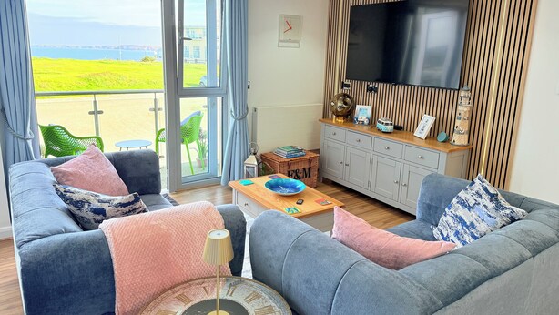 Ett vardagsrum med två grå soffor, ett soffbord, en tv och utsikt över havet genom stora fönster.