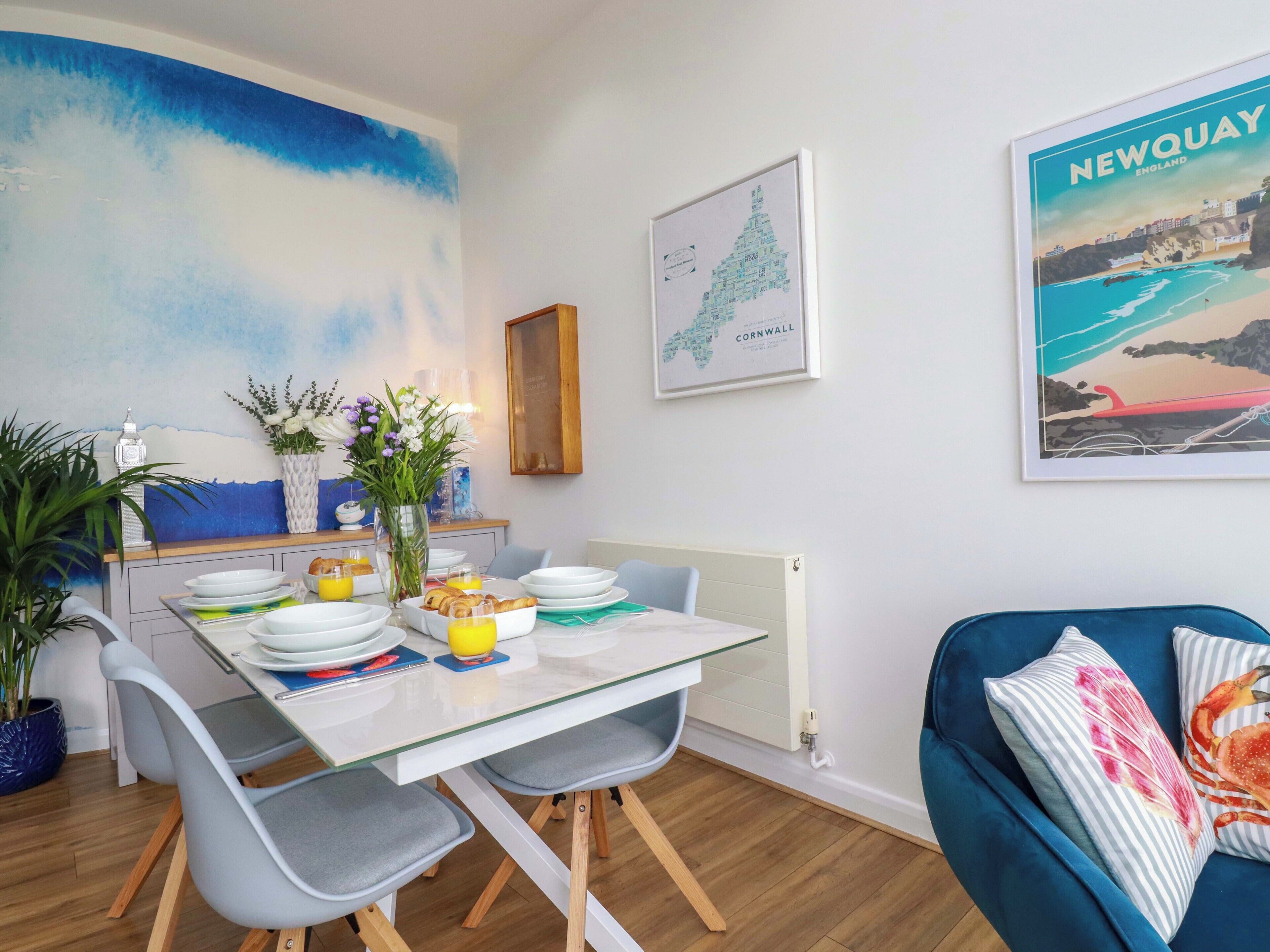 A dining area with a table set for breakfast, a blue sofa, and a wall with a map and a painting.