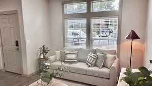Een woonkamer met een beige bank, een bijzettafeltje met decoratieve objecten en een vloerlamp.