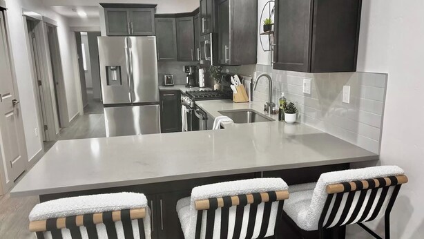 Een moderne keuken met donkere kastjes, roestvrijstalen apparatuur, een groot eiland met barkrukken en een betegelde spatwand.