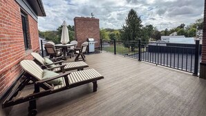 Une terrasse extérieure couverte, aménagée avec des chaises longues, une table et un mur en briques.