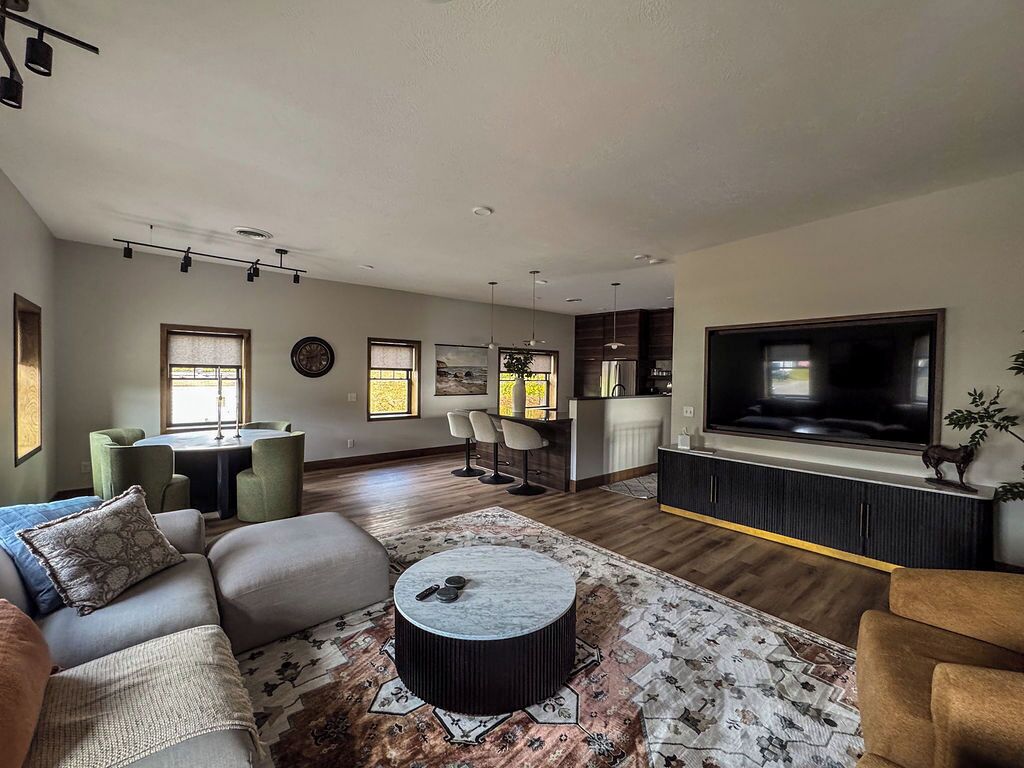 A modern living room with a sofa, coffee table, and TV. There is a dining area with chairs and a table.