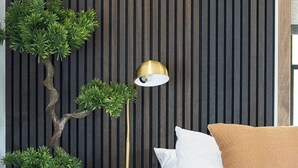 Une chambre à coucher avec un lit, des oreillers, une lampe sur pied et un bonsaï, le tout placé devant un mur à rayures.