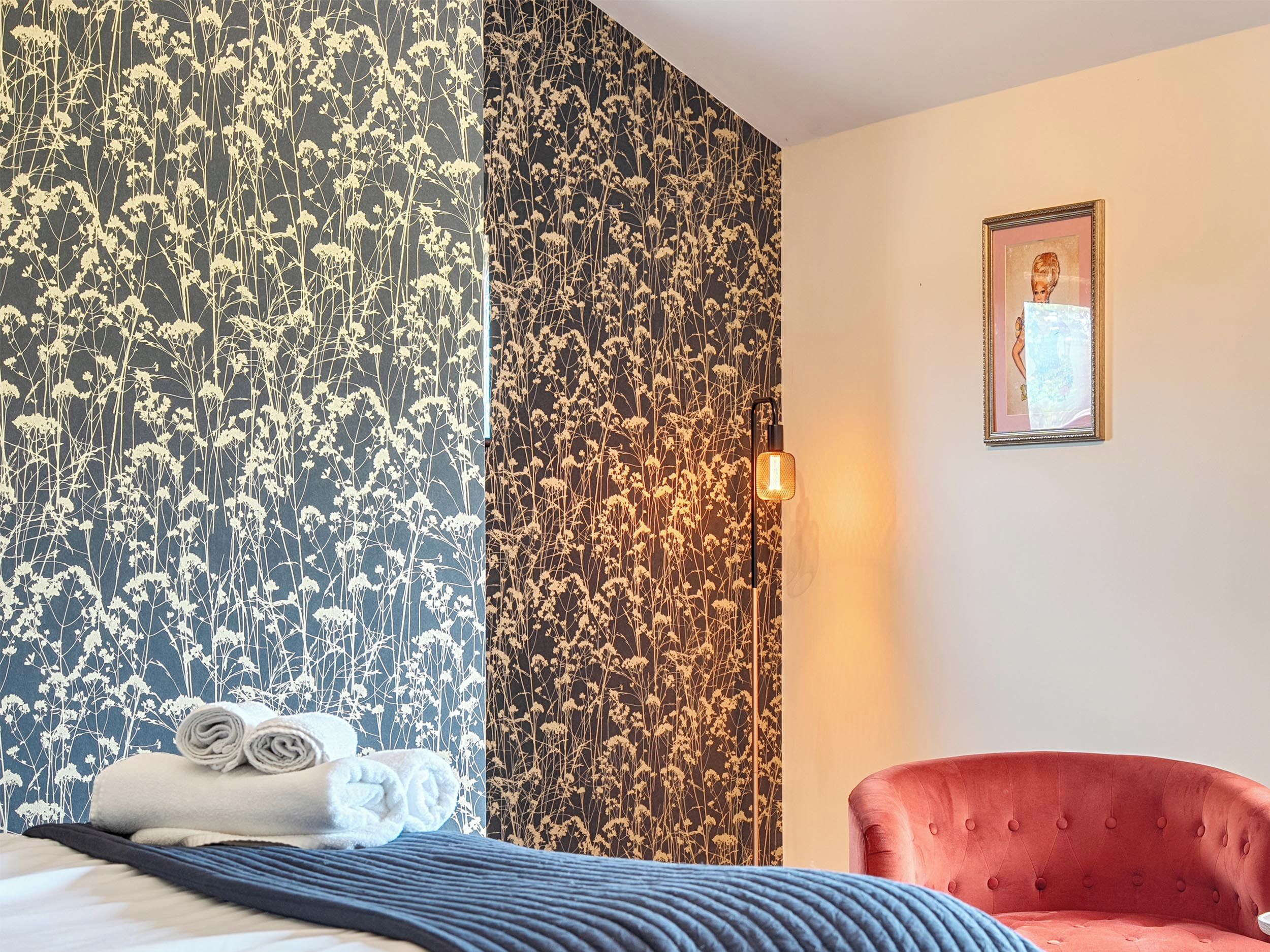 Una habitación de hotel con una cama, un sillón rojo y una pared con estampado floral.
