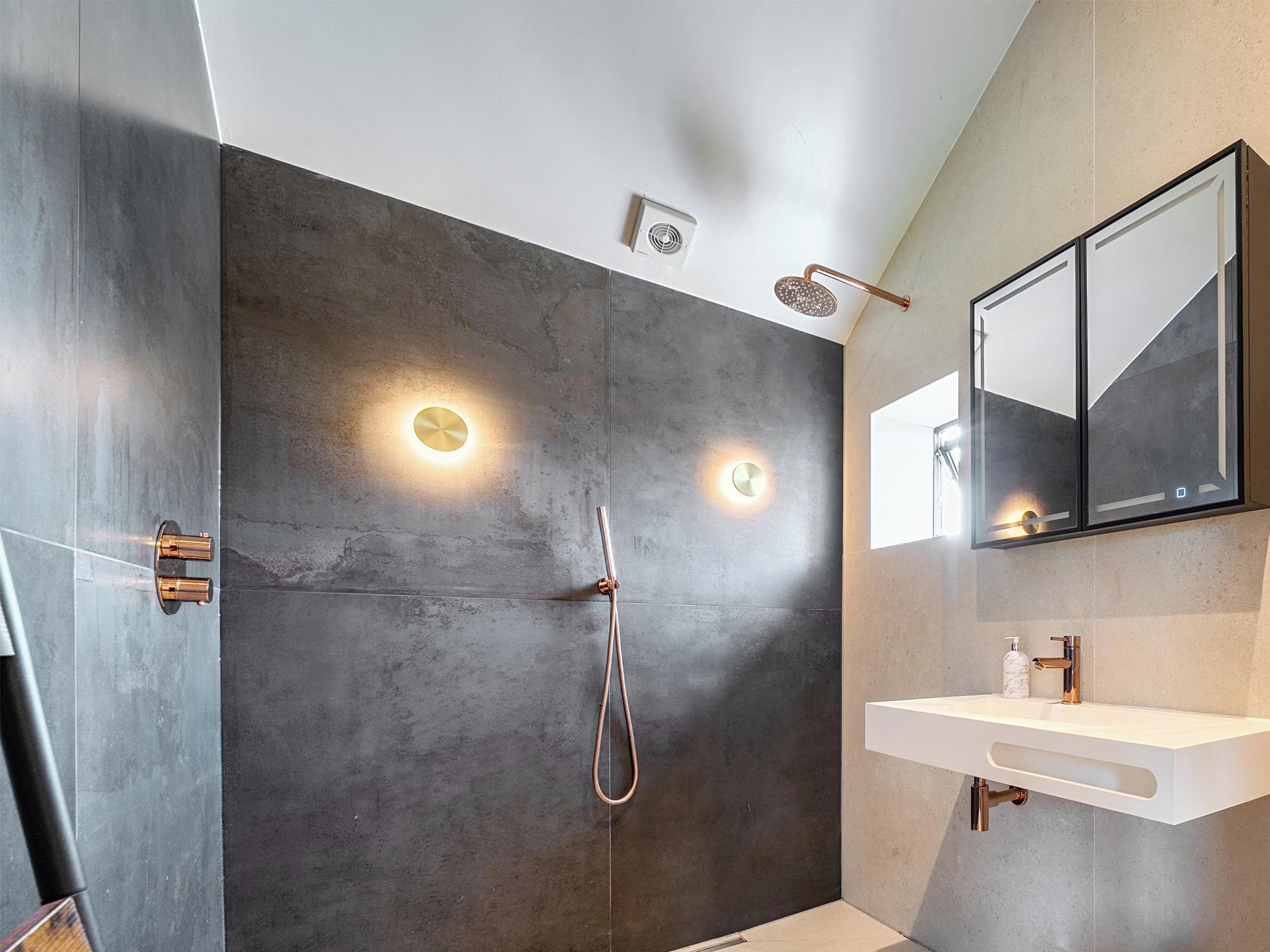 Un baño moderno con cabina de ducha, lavabo de pared y un espejo grande.