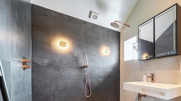 Un baño moderno con cabina de ducha, lavabo de pared y un espejo grande.