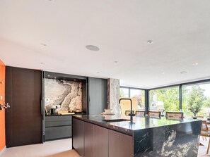 Cocina moderna con una isla de mármol, muebles oscuros y un amplio ventanal con vistas al exterior.