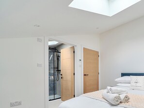 Un dormitorio con cama, puerta de madera, zona de ducha y tragaluz.